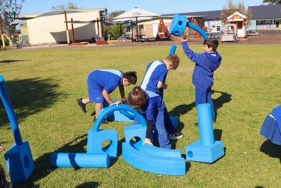 A group of kids playing with large blue objects outside